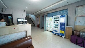 Zona de recepción con mostrador, área de descanso, escalera y máquina expendedora.