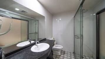 Un baño moderno con dos lavamanos, inodoro y ducha con mampara de vidrio.
