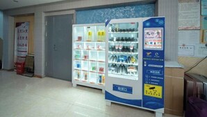Máquina expendedora con bebidas y aperitivos, una puerta cerrada y un tablón de anuncios.