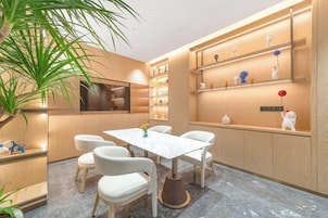 A modern dining area with a marble table and white chairs, surrounded by wooden walls and shelves with decorative items.