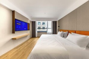 Une chambre d’hôtel avec un lit, un téléviseur fixé au mur, un plancher en bois et une vue sur les bâtiments environnants.