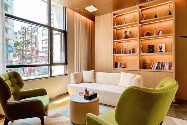 A modern living room with a sofa, two armchairs, a coffee table, and a bookshelf filled with books and decorative items. - Huaxi Hotel (Nayong)