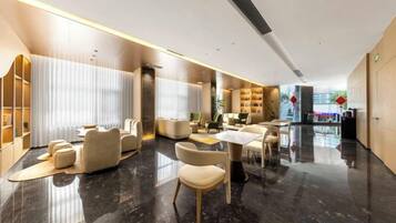 A modern hotel lobby with a marble floor, leather seating, and a reception desk.