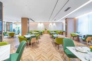 A modern dining area with green chairs, white tables, and a herringbone floor pattern.