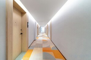 Ein Hotelgang mit Teppichböden, Holztüren und Deckenbeleuchtung.