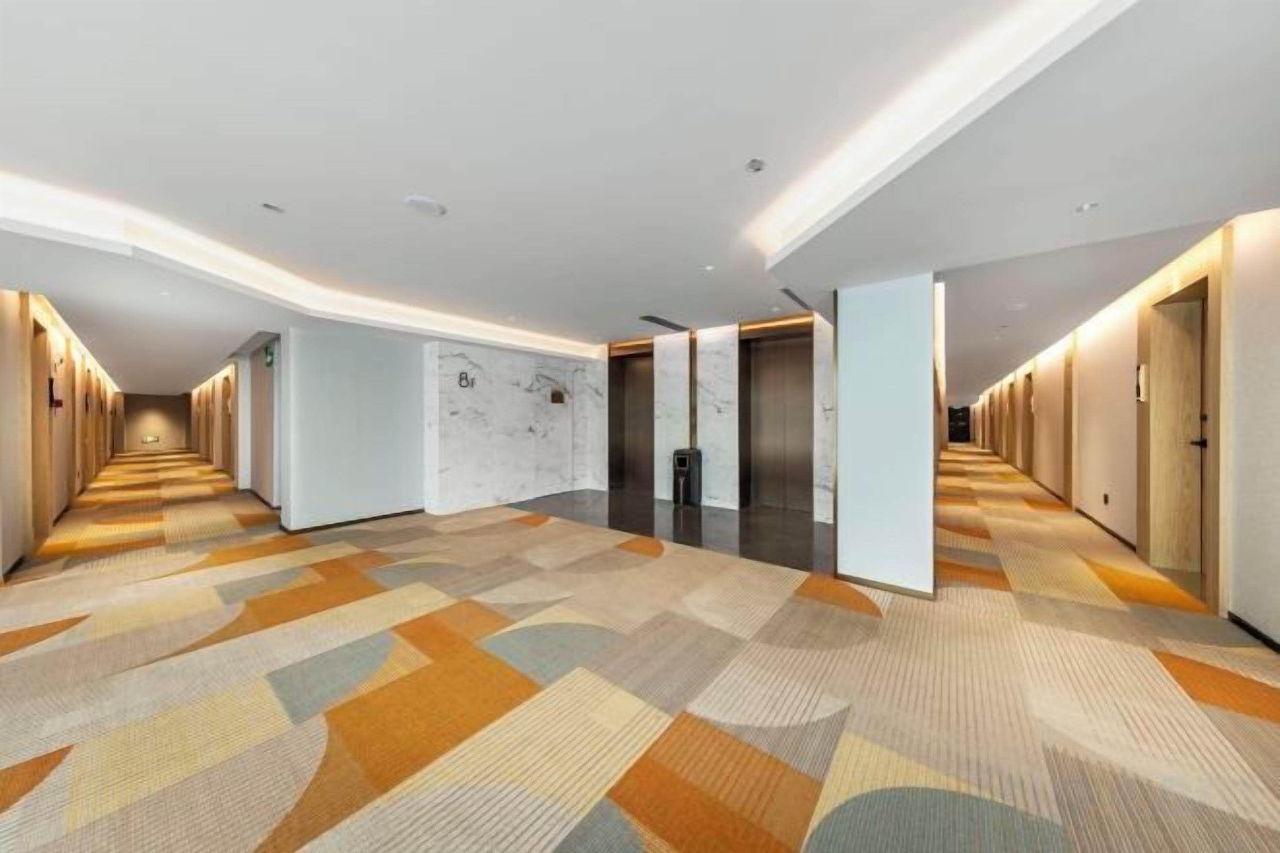 A hotel corridor with a patterned carpet, doors on both sides, and a marble wall.