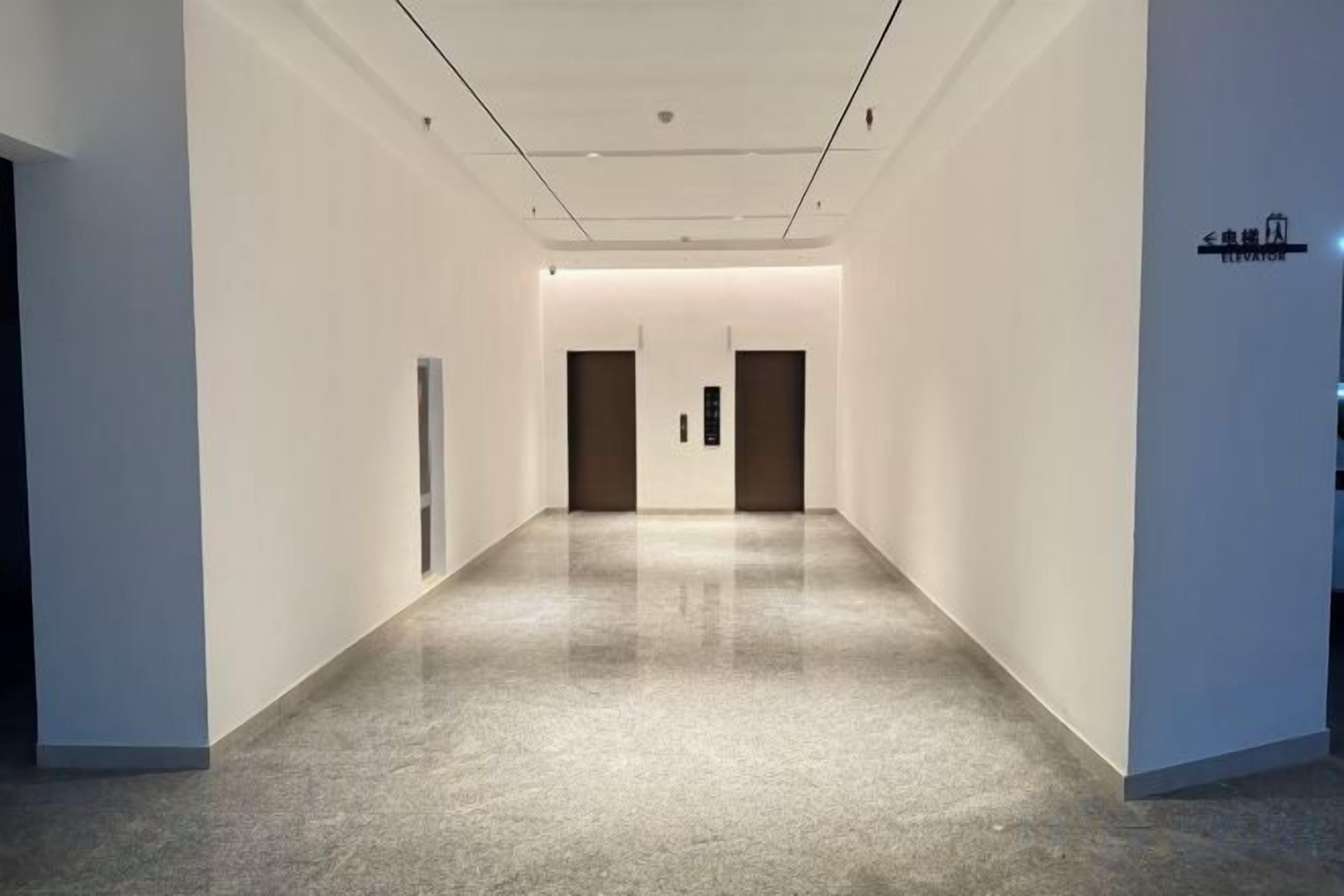 A corridor with a polished floor, white walls, and doors at the end.