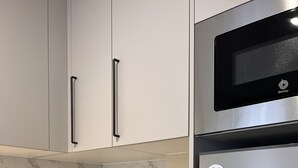 A modern kitchen with white cabinets, a black microwave, a stainless steel refrigerator, and a marble countertop. - Charming and bright T3 completely renovated, located 10 minutes walk from downtown. (Gijón)