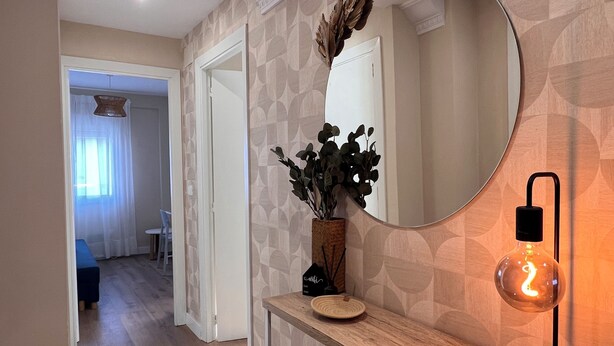 A hallway with a wooden console table, a round mirror, and a hanging light fixture. - Charming and bright T3 completely renovated, located 10 minutes walk from downtown. (Gijón)