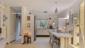 Une cuisine moderne avec des meubles blancs, un coin repas comprenant une table et des chaises, et une fenêtre donnant sur un paysage verdoyant.