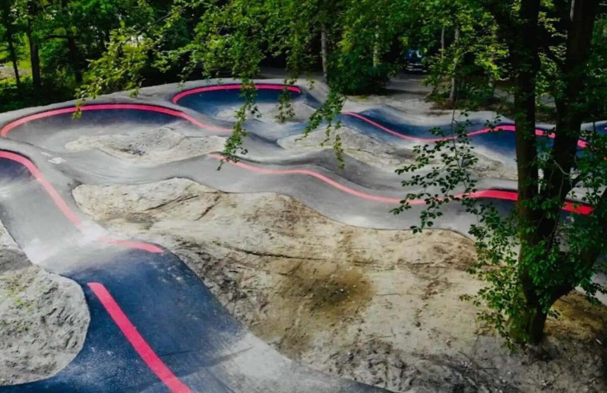 A winding outdoor track with red and blue painted lines, surrounded by trees.