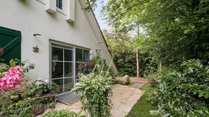 Une maison à l’extérieur blanc, avec une porte verte et une porte vitrée donnant sur un patio.