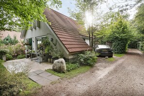 A house with a sloped roof, a gravel driveway, and a garden with various plants and flowers.