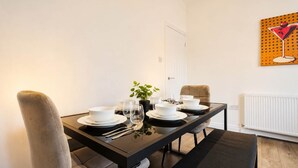 Ein Essbereich mit einem schwarzen Tisch, gedeckt für vier Personen, weißen Tellern, Schüsseln und Gläsern, einer Topfpflanze und einem Gemälde einer Martini-Glass auf der Wand.