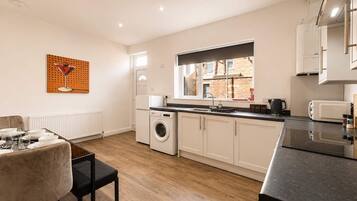 A modern kitchen with a built-in washing machine, a dining area with a table set for two, and a window providing natural light.