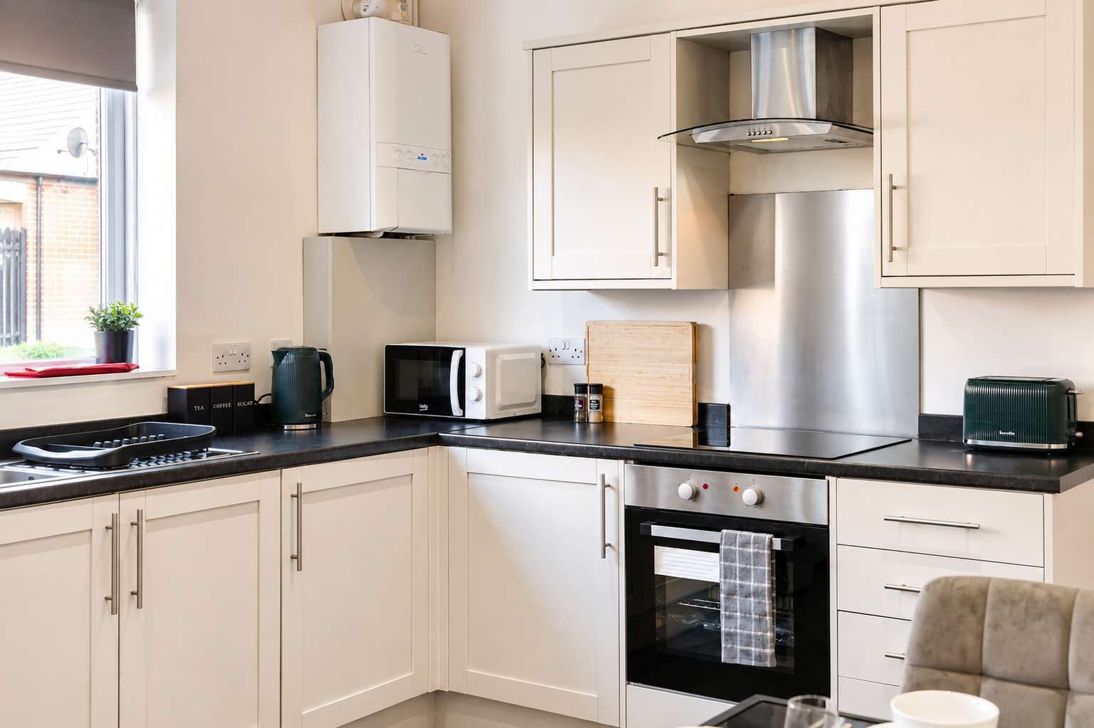 A modern kitchen with white cabinetry, a stainless steel range hood, a built-in oven, a microwave, and a toaster.