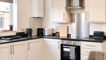 A modern kitchen with white cabinetry, a stainless steel range hood, a built-in oven, a microwave, and a toaster.