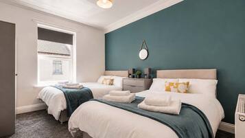 A hotel room with two beds, a window, a mirror, and a bedside table with a lamp.