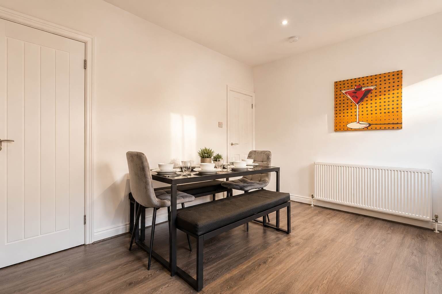 A dining area with a table set for two, a bench, and a radiator on the wall.