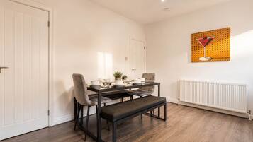 A dining area with a table set for two, a bench, and a radiator on the wall.