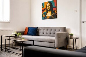 A living room with a grey sofa, a coffee table, a side table with a plant, and a painting of a famous artwork on the wall. - Spacious 3BR in Blyth | Sleeps 6 | By Stay With Us (Northumberland)