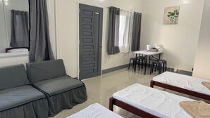 A hotel room with a grey sofa, two single beds, a small table with chairs, a mirror, and a window with grey curtains. - Helens Mountain Resort (Arakan)