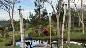 A circular seating area with two chairs and a fire pit, surrounded by a gravel path and a small pond, with trees and greenery in the background. - Helens Mountain Resort (Arakan)