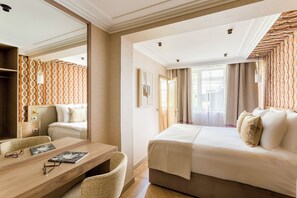 A hotel room with a large bed, a desk with a chair, a mirror, and a wardrobe.