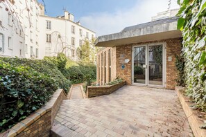 A courtyard with a brick pathway leading to a glass door entrance.