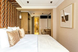 A hotel room with a large bed, a desk, a chair, and a TV.