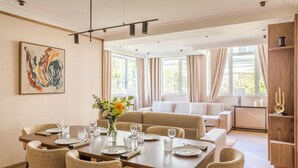 A modern dining area with a wooden table set for four, surrounded by beige upholstered chairs. - Merveil - Signature Suite - Tour Eiffel - Viala IV (Paris)