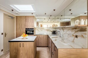 A modern kitchen with a central island, wooden cabinets, a built-in oven, and a marble countertop.