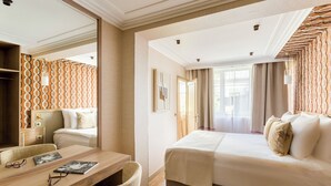 A hotel room with a large bed, a desk with a chair, a mirror, and a wardrobe. - Merveil - Signature Suite - Tour Eiffel - Viala IV (Paris)