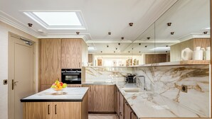 A modern kitchen with a central island, wooden cabinets, a built-in oven, and a marble countertop. - Merveil - Signature Suite - Tour Eiffel - Viala IV (Paris)