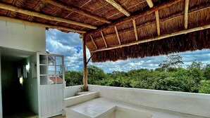 Una habitación moderna con techo de paja, un gran ventanal con vistas a la vegetación y un banco empotrado.