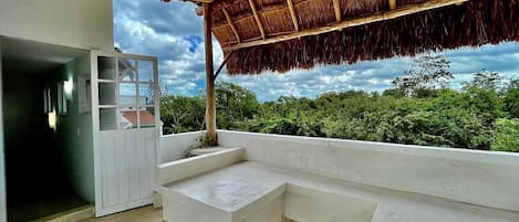 Una habitación moderna con techo de paja, un gran ventanal con vistas a la vegetación y un banco empotrado.