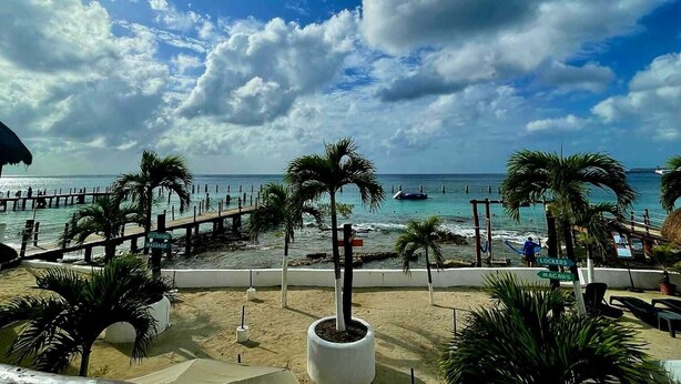 Vista de la playa con muelle, palmeras y un cartel que dice 'Masaje'.