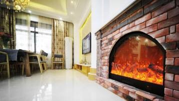 A living room with a brick fireplace, a dining area with a table and chairs, and a large window with curtains.