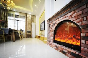 A living room with a brick fireplace, a dining area with a table and chairs, and a large window with curtains. - Tiantai Happiness Inn (Tiantai County)