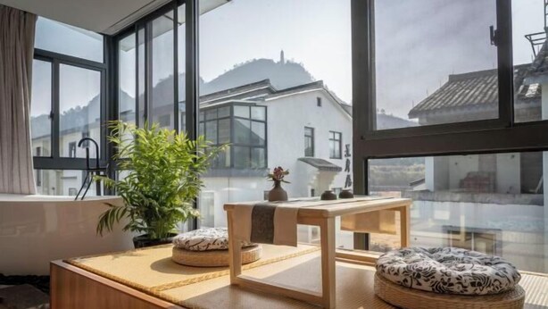 A modern room with large windows, a wooden table, a plant, and a traditional Japanese-style cushion. - Tiantai Happiness Inn (Tiantai County)