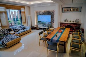 A modern living room with a sofa set, dining table, and chairs, a flat-screen TV, and a fireplace.