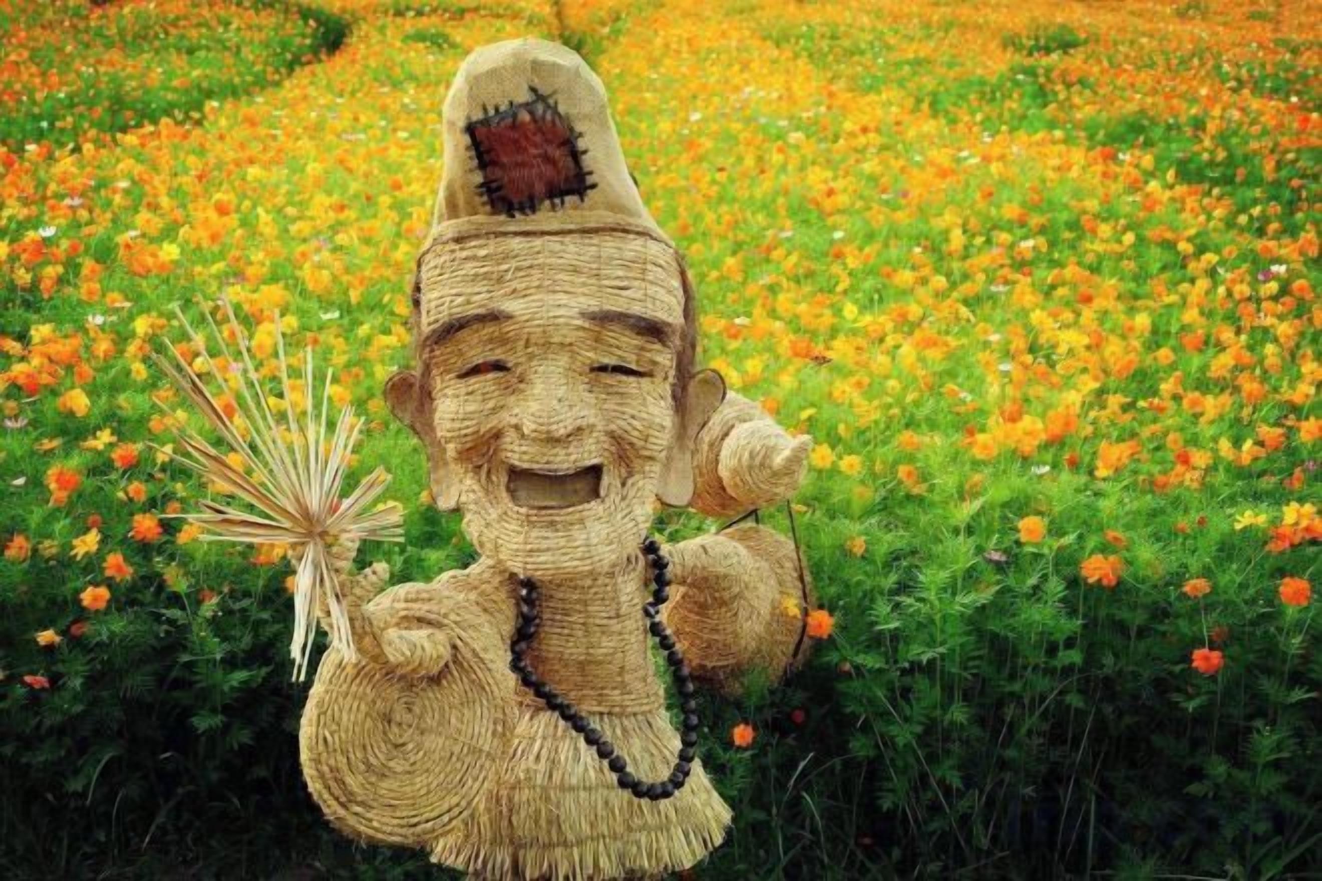 Una escultura de una figura sosteniendo un abanico y un collar de cuentas, con un campo de flores naranjas de fondo.