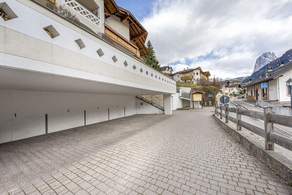A pedestrian pathway with a white building featuring a wooden balcony and a mountain backdrop.