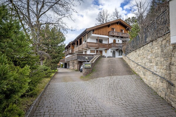 A traditional wooden building with balconies, a stone wall, and a paved pathway.