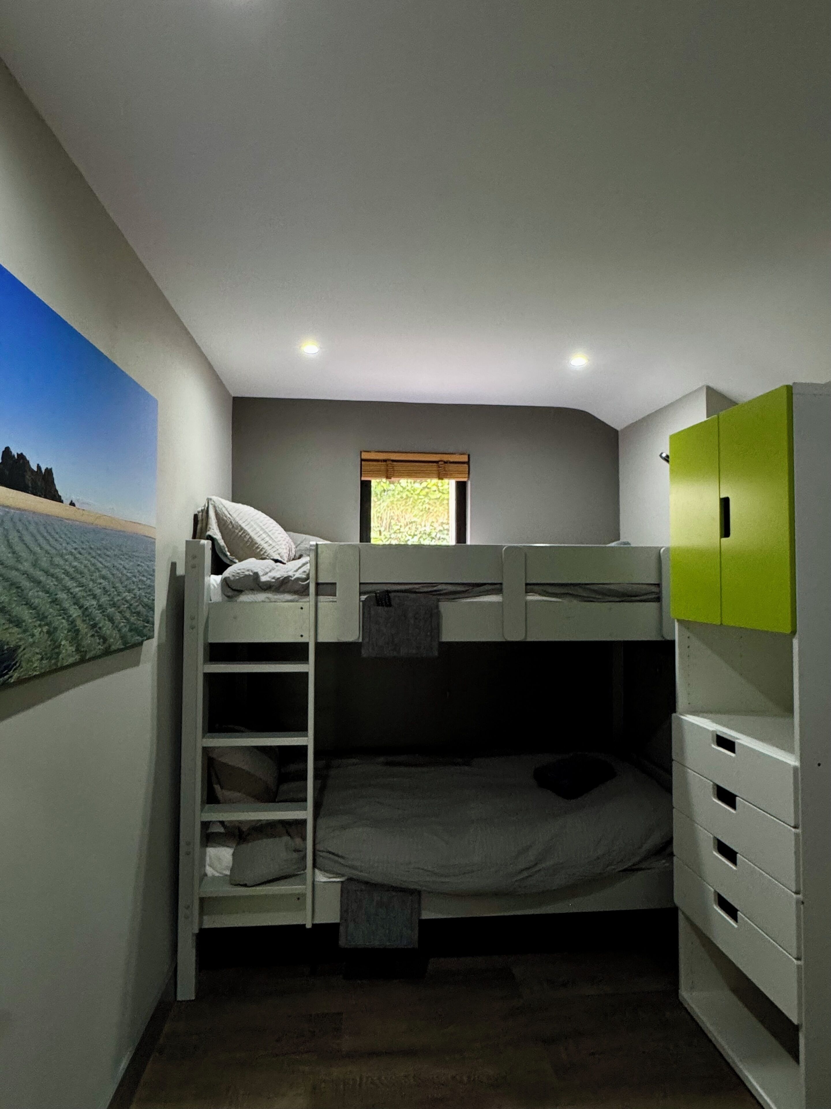 Ein Schlafraum mit Etagenbett, einer Leiter, einem Fenster und einem grünen Kleiderschrank.