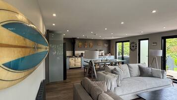 A modern living room with a sofa, a dining table, and a kitchen in the background.