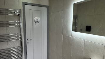 Um banheiro moderno com porta branca, porta-toalhas, rolo de papel higiênico e espelho na parede.