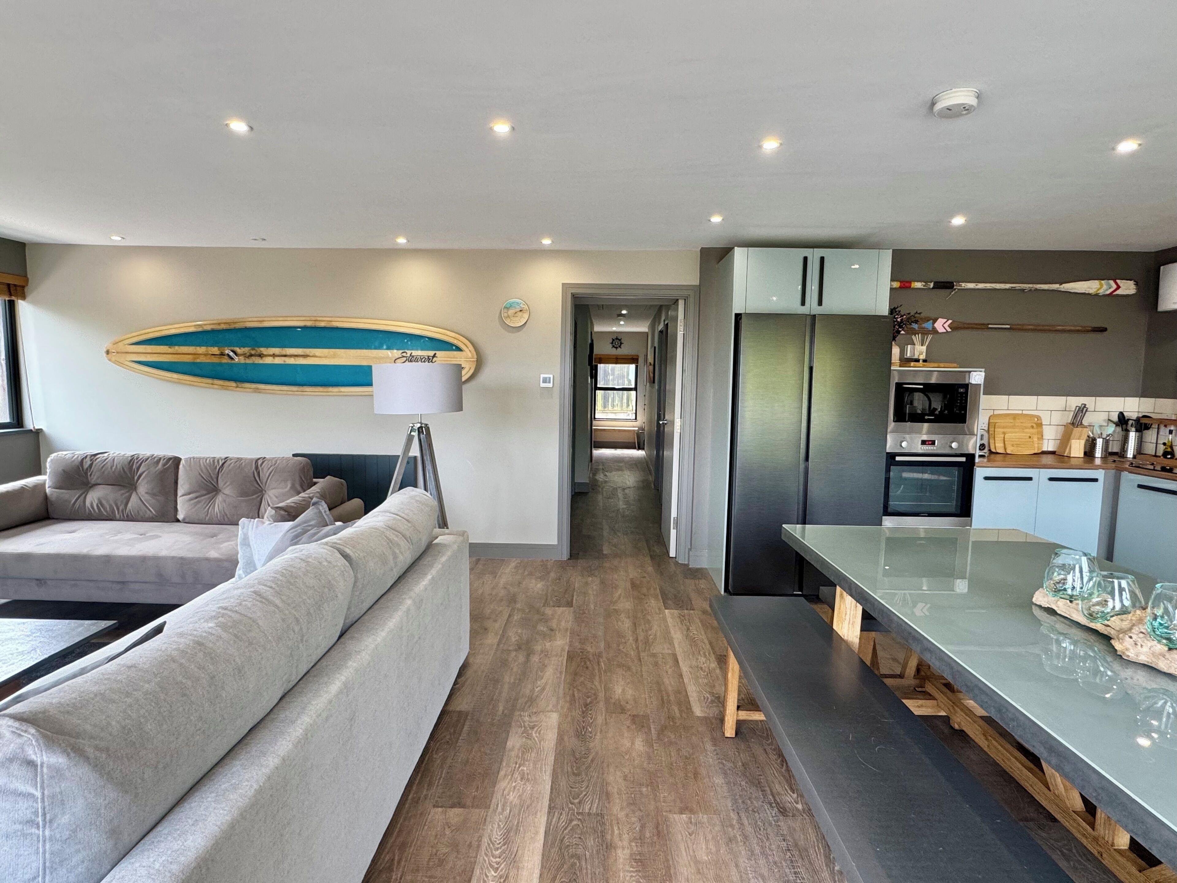 A modern living room with a sofa, a dining area with a bench, and a kitchen with appliances.