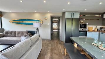 A modern living room with a sofa, a dining area with a bench, and a kitchen with appliances.