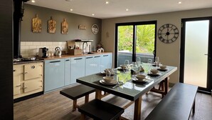 A modern kitchen with light blue cabinets, a black countertop, and a dining area with a glass table set for four. - Uno Moor Side (Carbis Bay)
